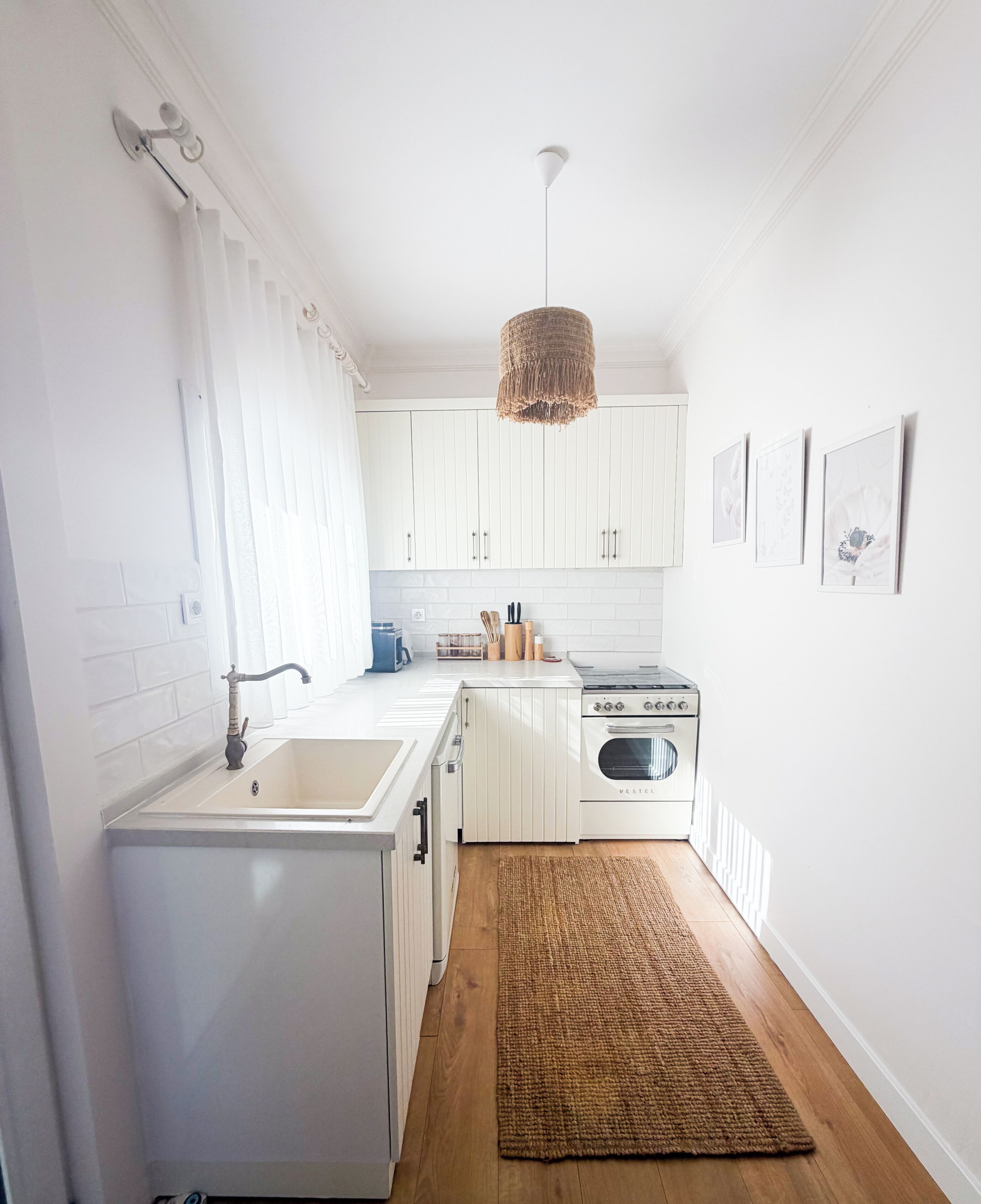 A compact kitchen with white cabinetry, a stove, a sink, and a hanging light fixture.