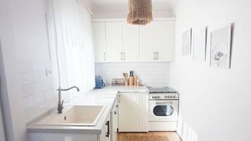 A compact kitchen with white cabinetry, a stove, a sink, and a hanging light fixture.