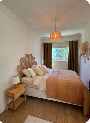 Une chambre à coucher comprenant un lit, une table de chevet, une lampe, une fenêtre avec des rideaux et un ventilateur suspendu.