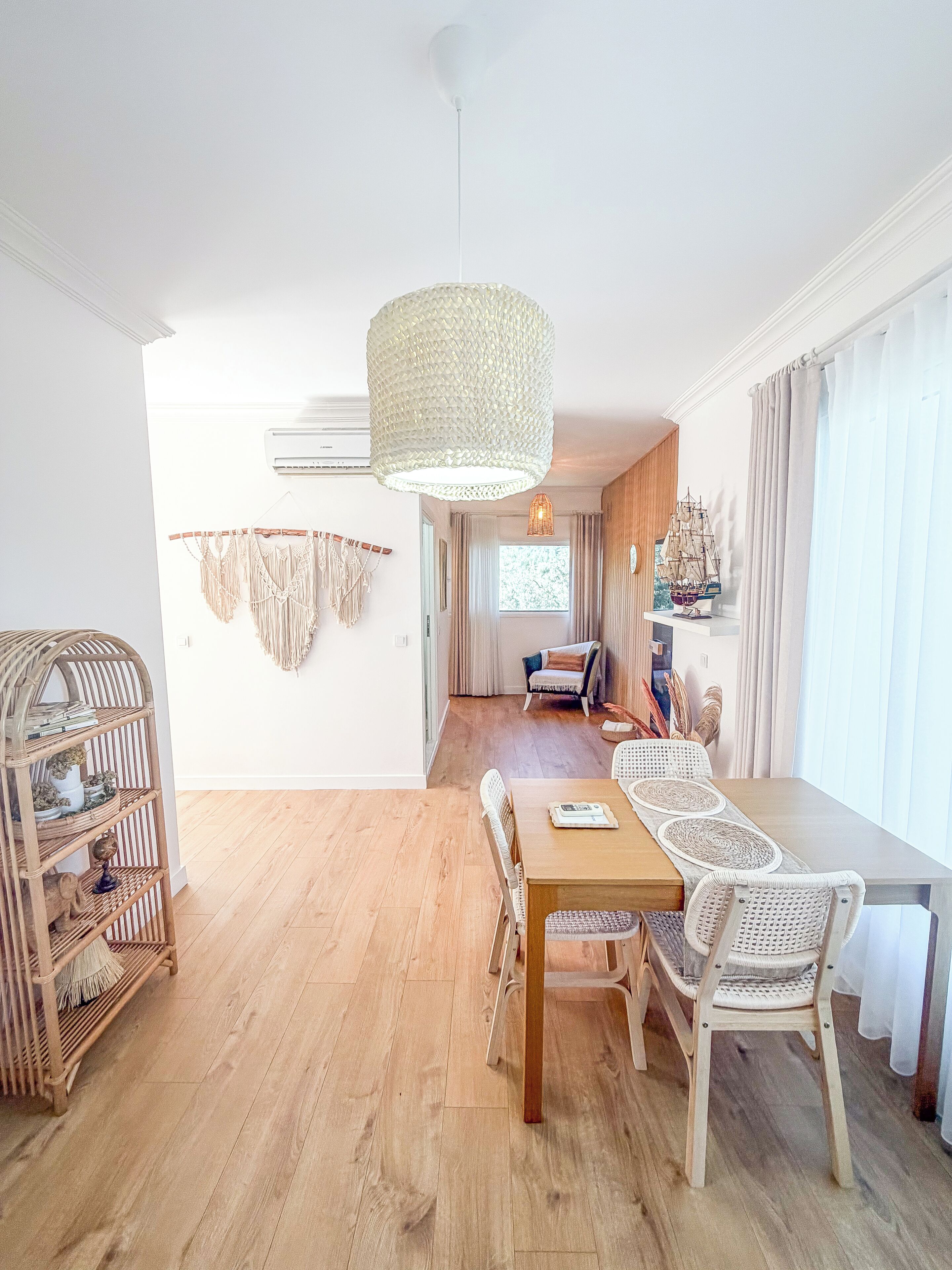 Un coin repas avec une table en bois et des chaises en osier, un luminaire suspendu et une décoration murale en macramé.