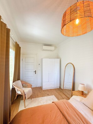 A bedroom with a bed, a chair, a wardrobe, a mirror, and a hanging light fixture. - Casa Del Olivia (Seferihisar)