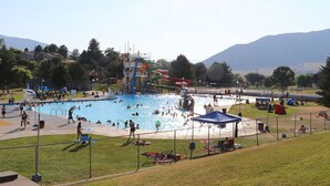Piscina pública con tobogán de agua, rodeada de zonas verdes y árboles.