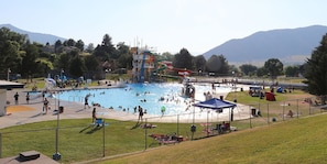 A public swimming pool with a water slide and a fenced area with picnic tables.