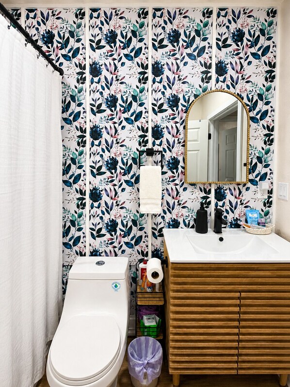 Un baño con inodoro, lavabo, espejo y papel tapiz con motivos florales.