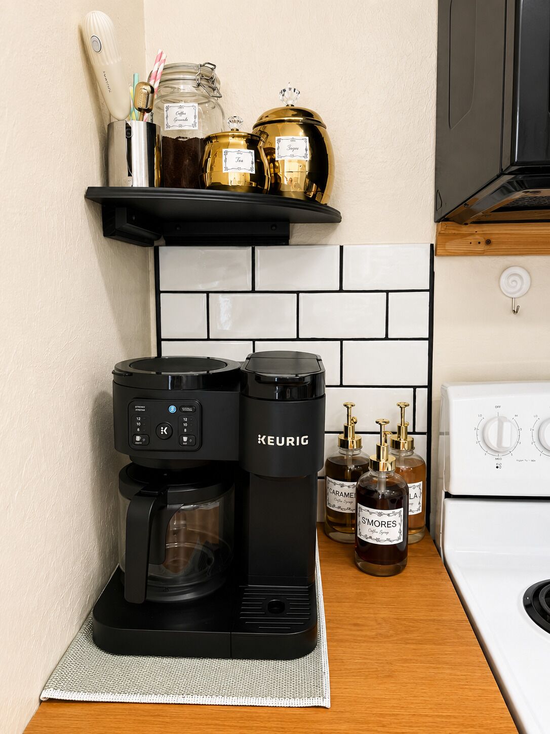 A coffee maker, a kettle, and two bottles of syrup on a kitchen counter.