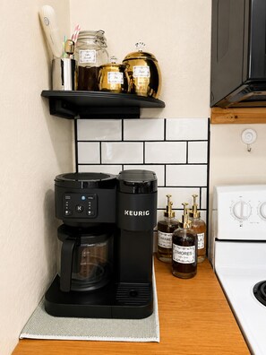 Una cafetera, un hervidor y dos botellas de sirope sobre una encimera de cocina.