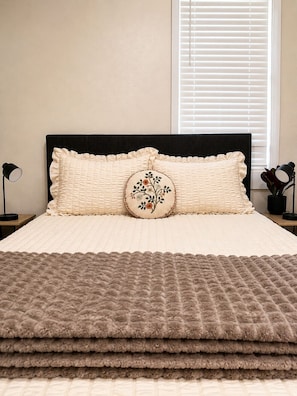 A neatly made bed with a quilted headboard, a decorative pillow, and a brown blanket.