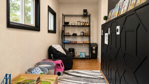 Una habitación con zona de juegos, un mueble de almacenamiento negro, una estantería y una ventana.