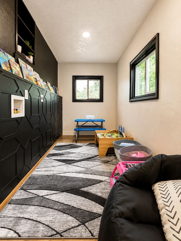 A room with a black geometric wall, a blue table, a window, and a black sofa.
