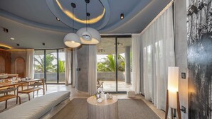 En moderne hotellobby med et rundt træbord, siddeområde og store vinduer med gardiner.