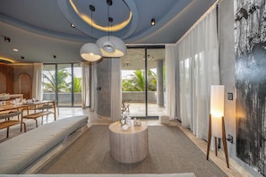 A modern hotel lobby with a round wooden table, seating area, and large windows with curtains. - Oceanfront 4BR Duplex in Maiim Tankah w/Pool & Gym (Tulum)