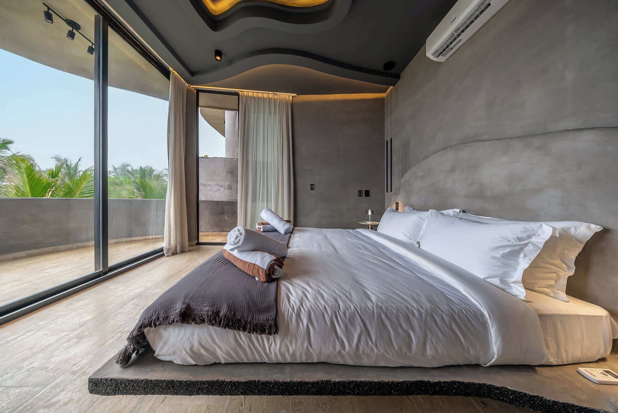 Ein modernes Schlafzimmer mit einem großen Bett, Blick durch eine Glastür und einer einzigartigen Deckenkonstruktion.