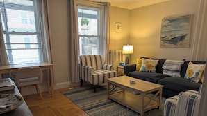 En stue med sofa, lænestole, et sofabord, en lampe og et billede på væggen.