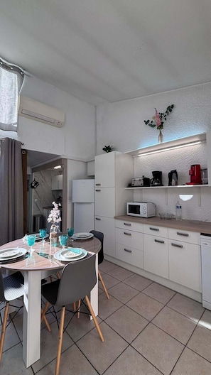 A modern kitchen with white cabinets, a microwave, a coffee maker, and a dining area with a table set for two. - Air-conditioned house 64 m2 Le Barcarès 100 m from the beach for 6 adults + 1 baby (Le Barcarès)