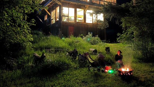 A two-story wooden house with a balcony, surrounded by trees and a grassy area. - Thunderbird Treehouse, a cozy artisan built home overlooking Mt Hood. (White Salmon)