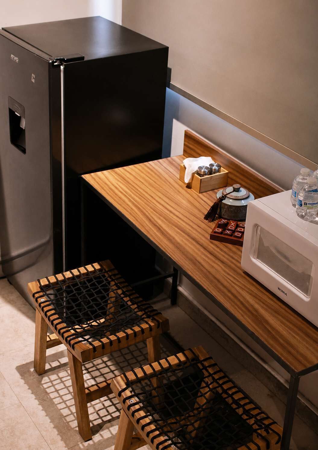 Eine kleine Küche mit einem schwarzen Kühlschrank, einer Mikrowelle und einem Holztisch mit zwei Hockern.
