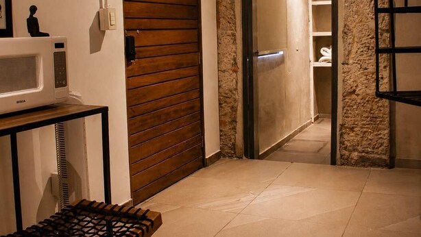 Une pièce avec une porte en bois, un micro-ondes blanc, une petite table avec une chaise en osier et un mur en pierre.