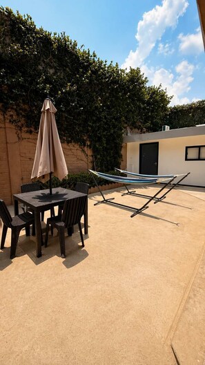 An outdoor patio with a table and chairs, a hammock, and a covered umbrella.