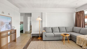Una sala de estar moderna con un sofá gris, una lámpara de pie, una pequeña mesa redonda y un cuadro en un mueble bajo de madera.