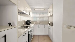 Una cocina compacta con armarios blancos, una estufa a gas, un fregadero y una ventana con persianas.