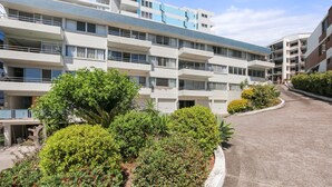 Un edificio residencial de varios pisos con balcones, entrada pavimentada y jardines.