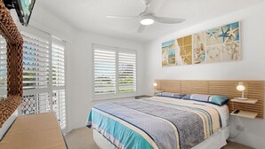 Ein Schlafzimmer mit Bett, Deckenventilator, Fenster mit Jalousien, einem Wandbild und einem Nachttisch mit Lampe.