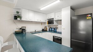 A modern kitchen with white cabinets, a black refrigerator, and a blue countertop.
