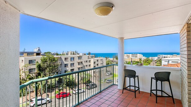 A balcony with a view of the sea, a tiled floor, and two chairs.