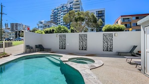 A swimming pool with a curved design, a white wall with decorative panels, and a view of surrounding buildings.