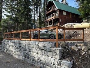 Eine Holzhütte mit einer Steinsichtmauer, einer Holzterrasse und einem geparkten Fahrzeug davor.