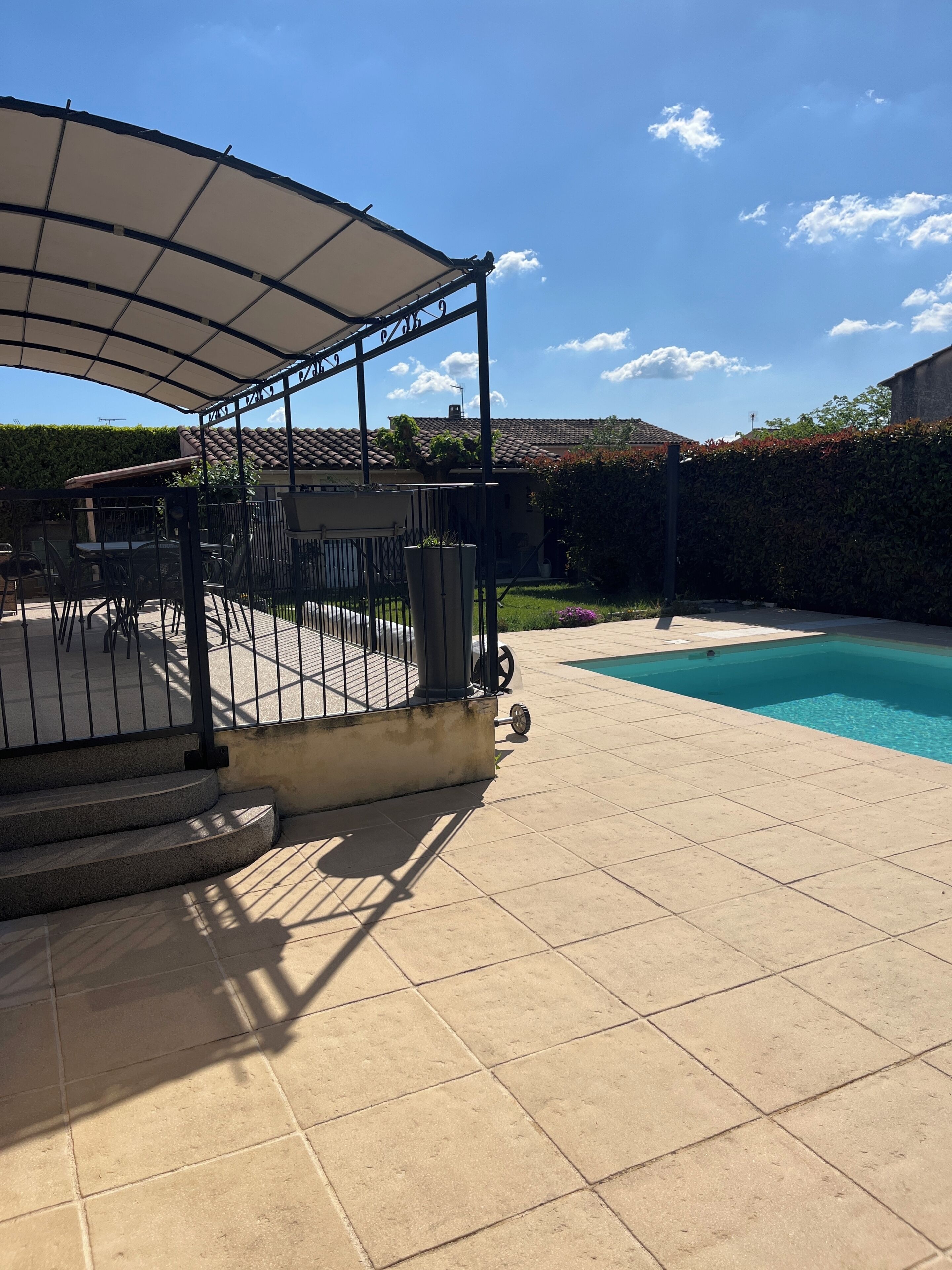 A patio area with a pool, a covered seating area, and a hedge.
