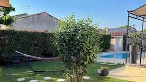 A backyard with a swimming pool, a hammock, and a small tree. - A single-storey house in a quiet subdivision with swimming pool and parking. (Manduel)