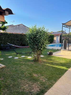 Ein Garten mit Pool, Hängematte und einem kleinen Baum.
