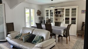 A living room with a sofa, dining table, chairs, and a bookshelf. - A single-storey house in a quiet subdivision with swimming pool and parking. (Manduel)