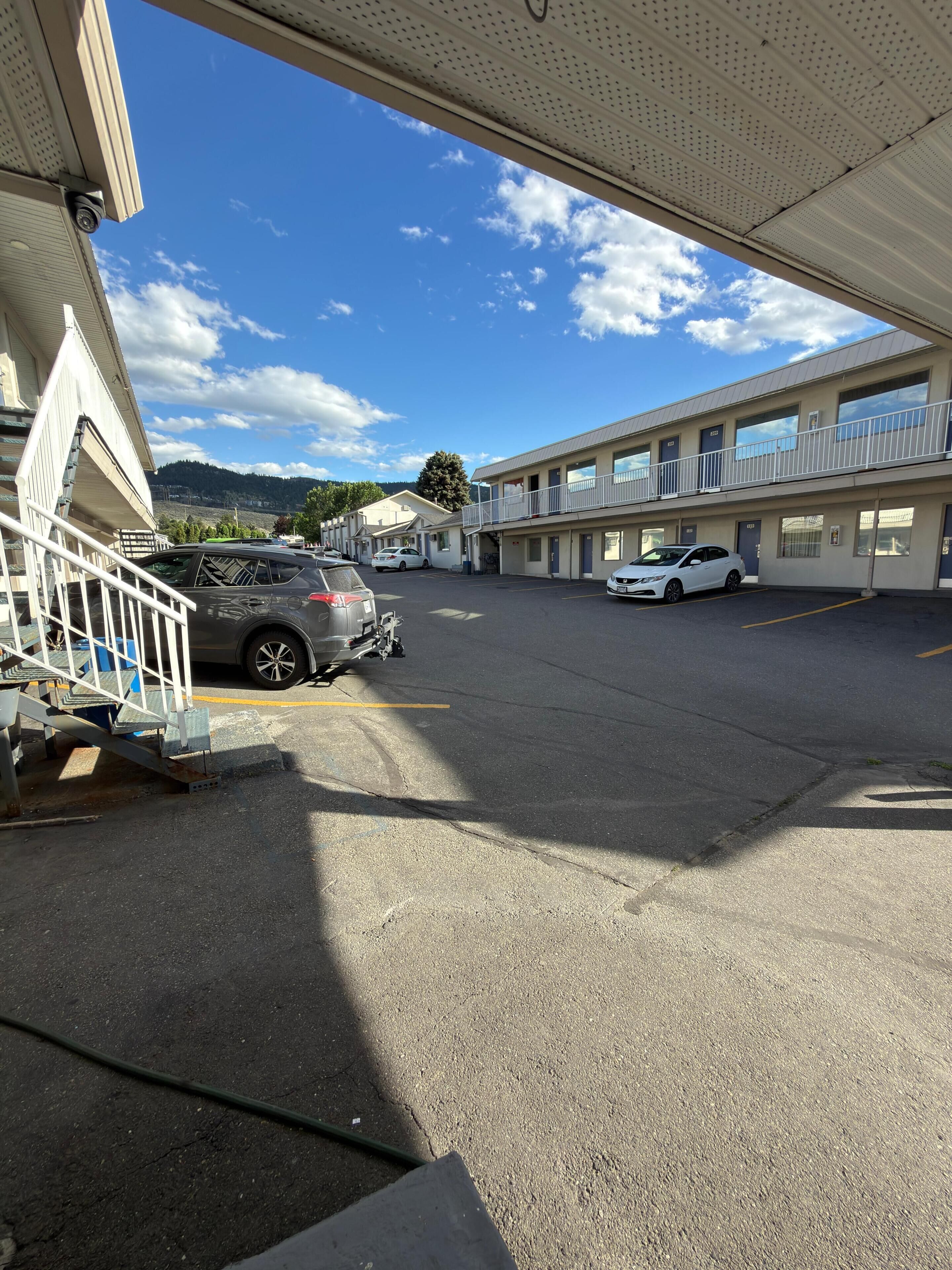 A motel with a parking lot, a covered walkway, and a mountain view in the background.