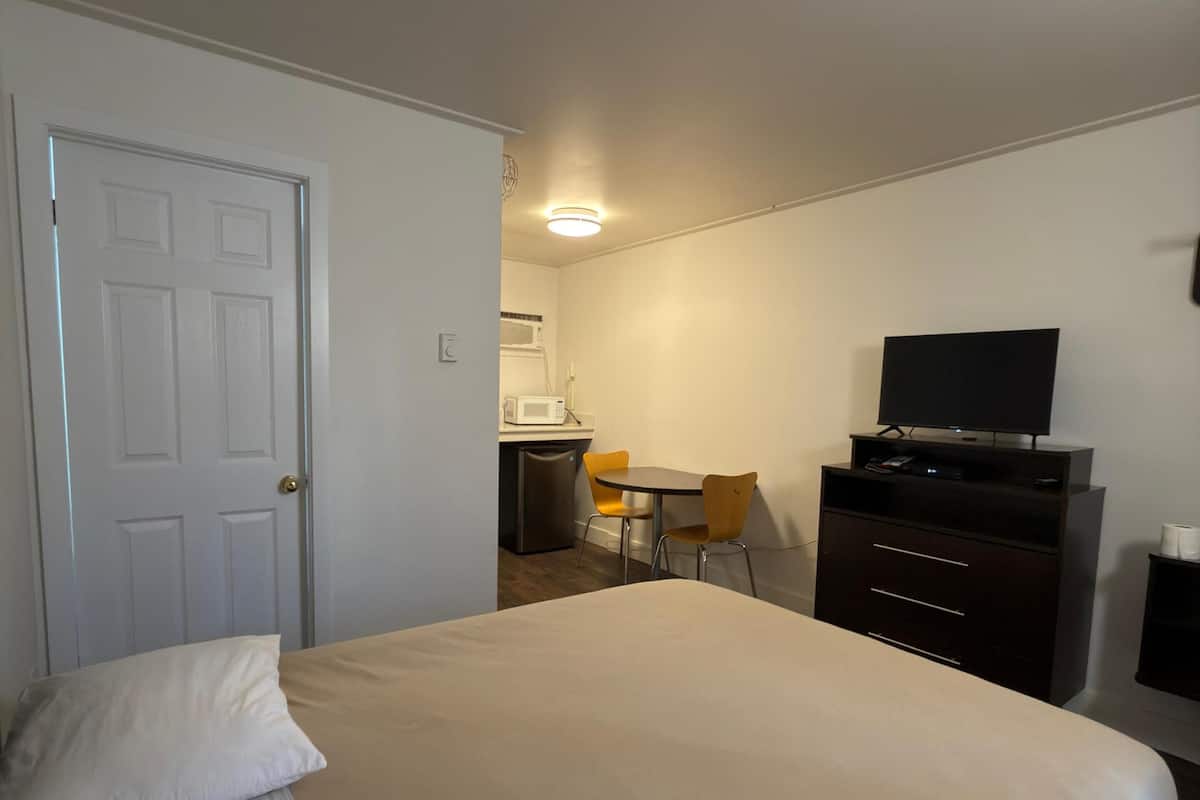 A bedroom with a bed, a desk with a chair, a television, and a microwave.