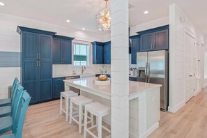 Eine moderne Küche mit blauen Schränken, einer großen Kochinsel mit Hockern und einem Edelstahl-Kühlschrank.