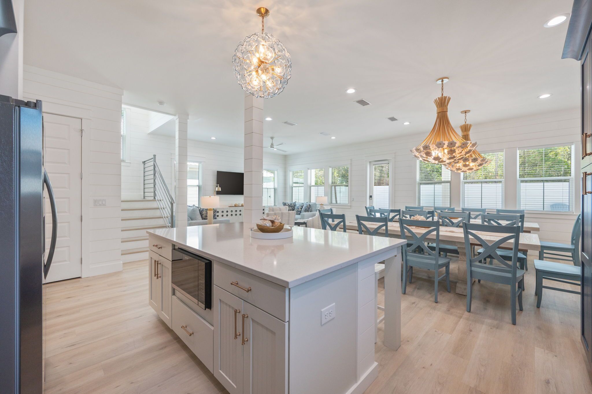 A spacious kitchen with a central island, modern pendant lights, and a dining area with chairs and tables.