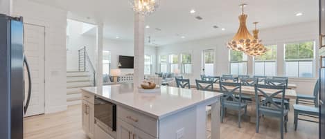 A spacious kitchen with a central island, modern pendant lights, and a dining area with chairs and tables.