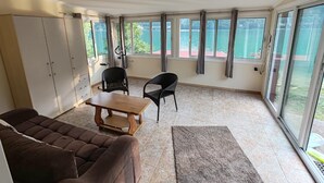 A room with a sofa, a table, chairs, a view of a lake, and a sliding glass door. - Lake House Perucac (Rađenovići)