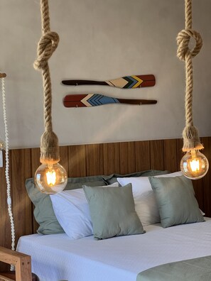 Ein Bett mit zwei hängenden Leuchten, einem Holz-Kopfteil und zwei dekorativen Holzschlägern an der Wand.