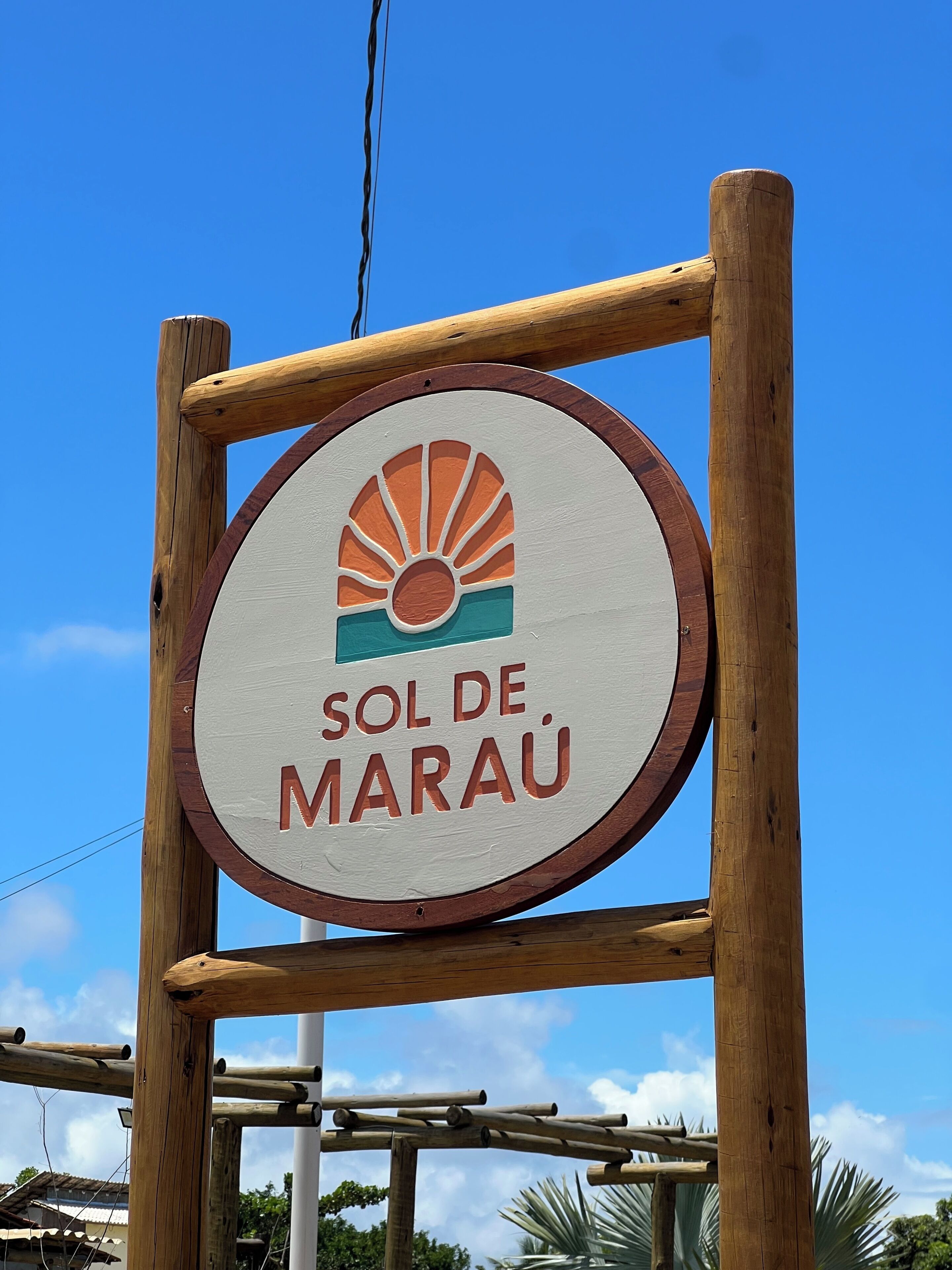Un letrero de madera con un diseño circular y el texto 'SOL DE MARAU' sobre un cielo azul despejado.