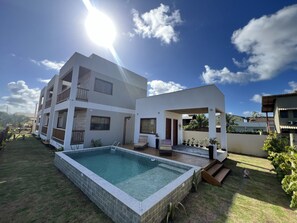 Ein modernes Mehrfamilienhaus mit Schwimmbad, Sitzgelegenheiten im Freien und einer überdachten Terrasse.