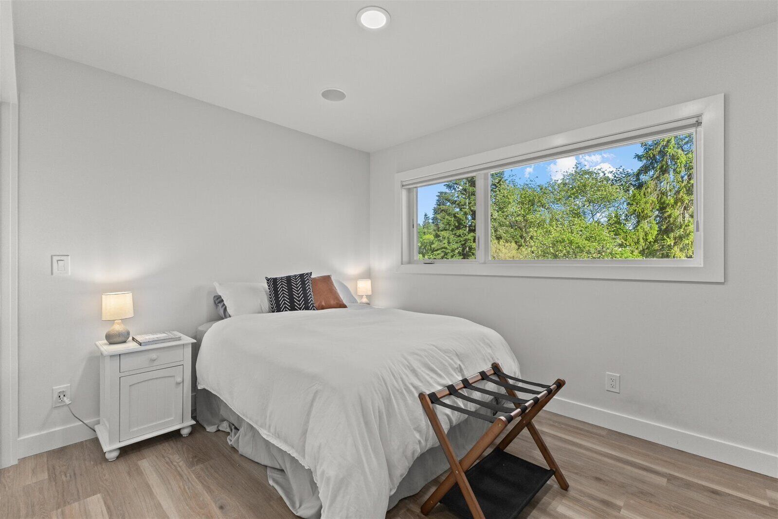 A bedroom with a bed, bedside lamps, a window with a view of trees, and a wooden floor.
