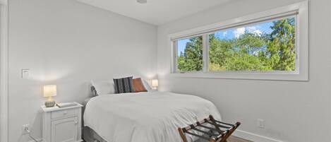 A bedroom with a bed, bedside lamps, a window with a view of trees, and a wooden floor.