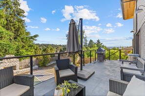 Eine Terrassenanlage im Freien mit Korbmöbeln, einem Grill und Blick auf die umliegende Bepflanzung.