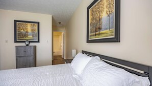A hotel room with a bed, a wardrobe, a bathroom, and two framed paintings on the walls.