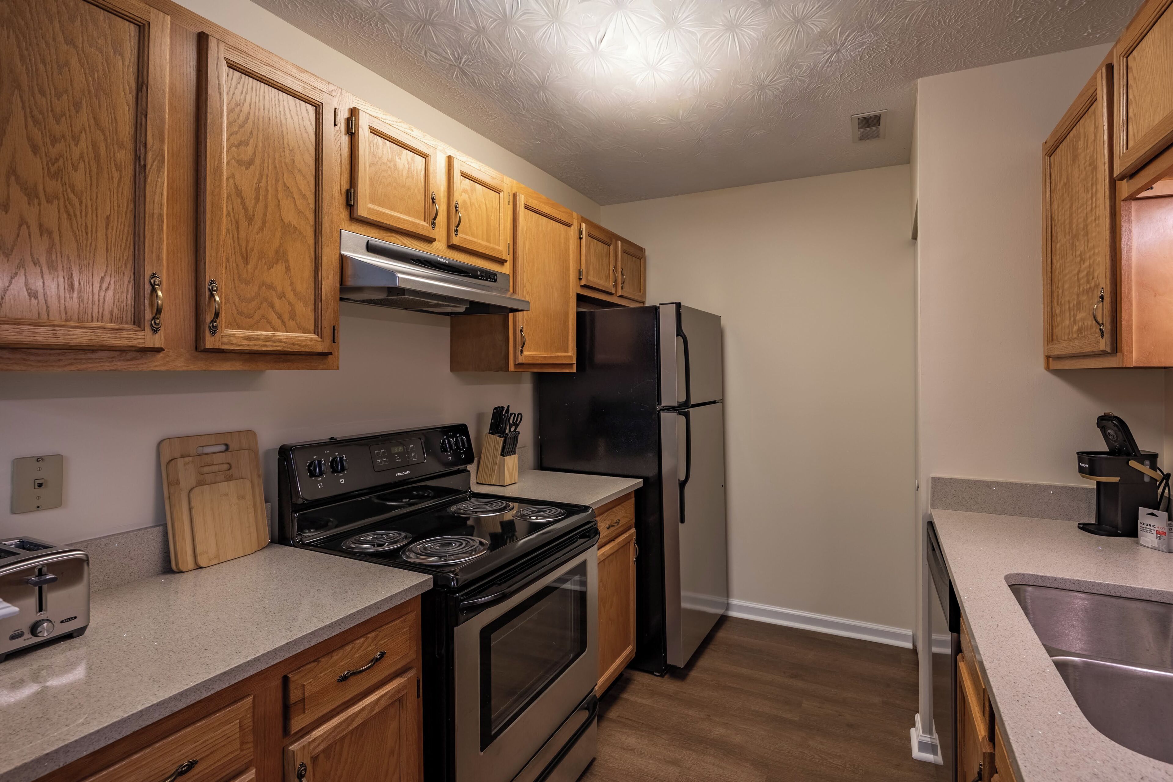 A kitchen with wooden cabinets, a stainless steel refrigerator, a stove, and a countertop with a toaster.