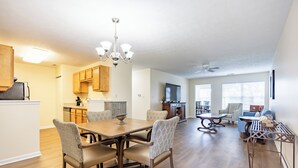A spacious kitchen with wooden cabinets, a dining area with a wooden table and patterned chairs, and a living area with a sofa and a TV.