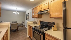 A kitchen with wooden cabinets, a stove, a refrigerator, and a dining area with chairs and a table.